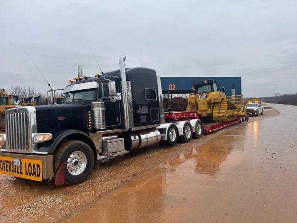 A semi truck is carrying a bulldozer down a dirt road.