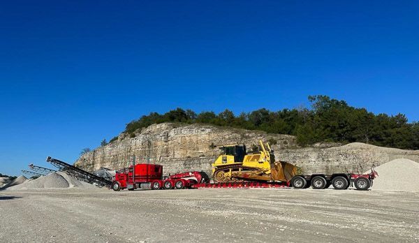 A bulldozer is being transported on a trailer in a quarry.