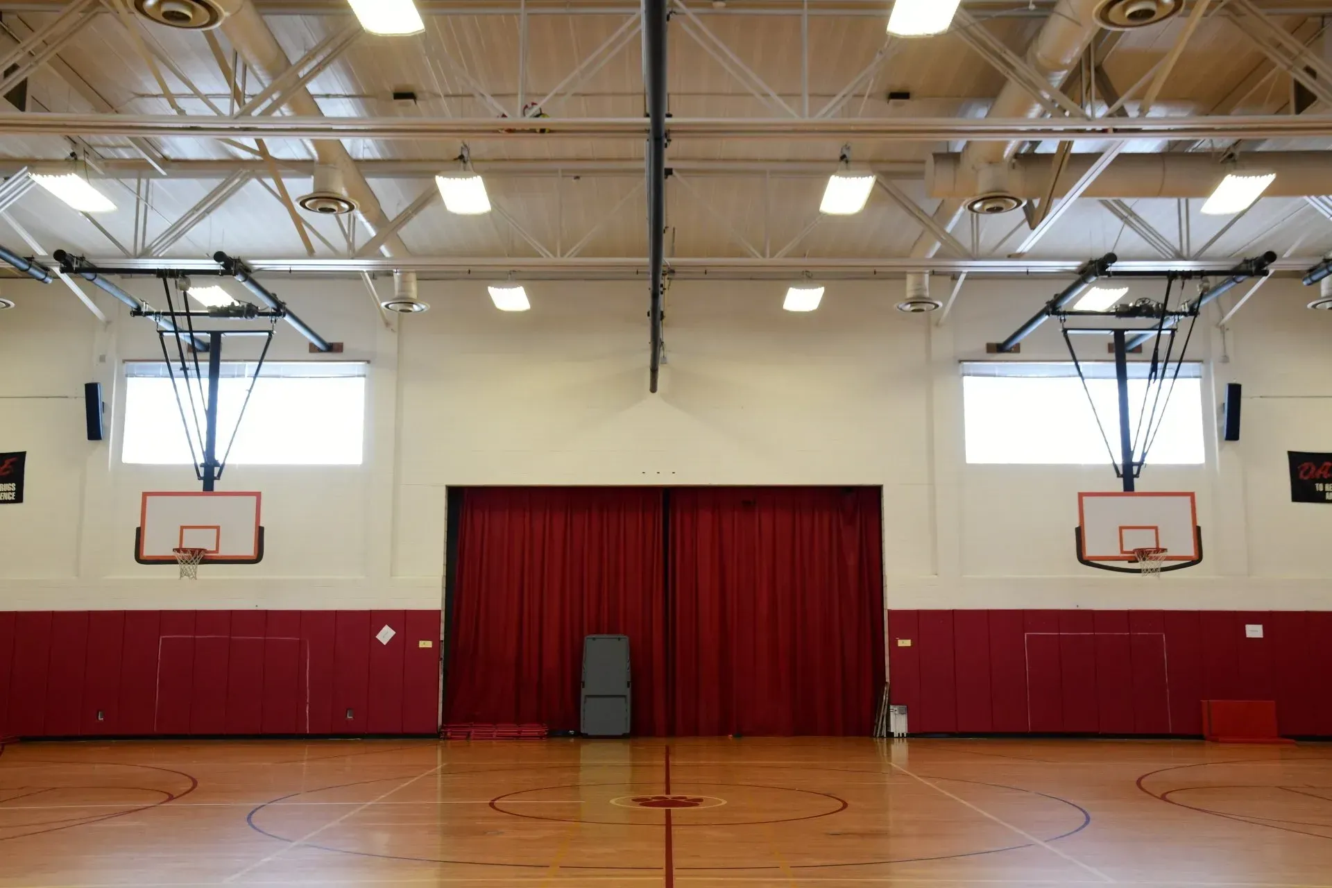 An empty gym with a basketball hoop and red curtains