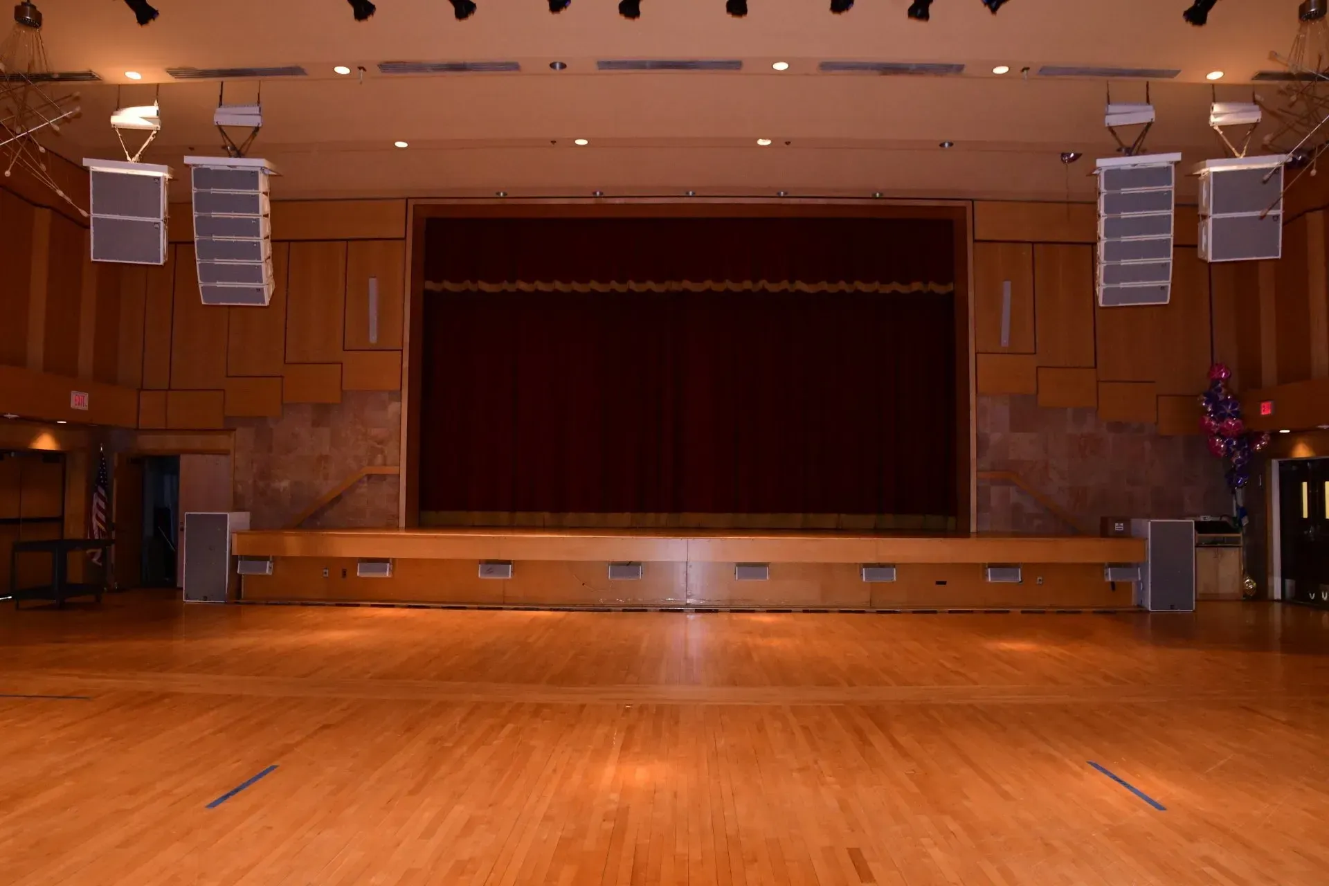 An empty auditorium with a wooden floor and a red curtain