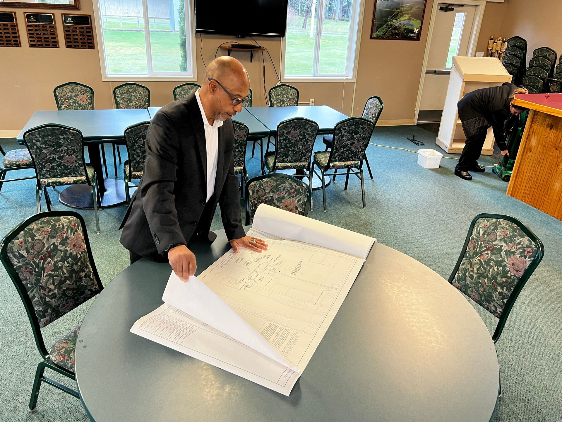 A man in a suit is looking at a blueprint on a table