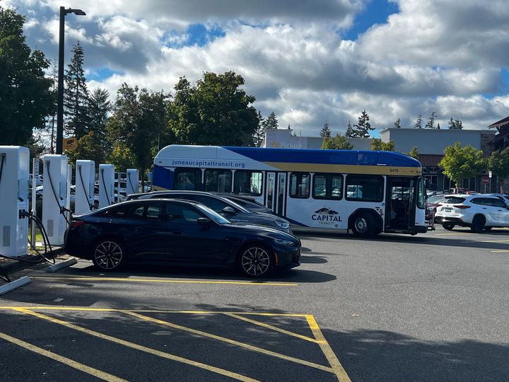 A blue and white bus is parked next to a black car in a parking lot.