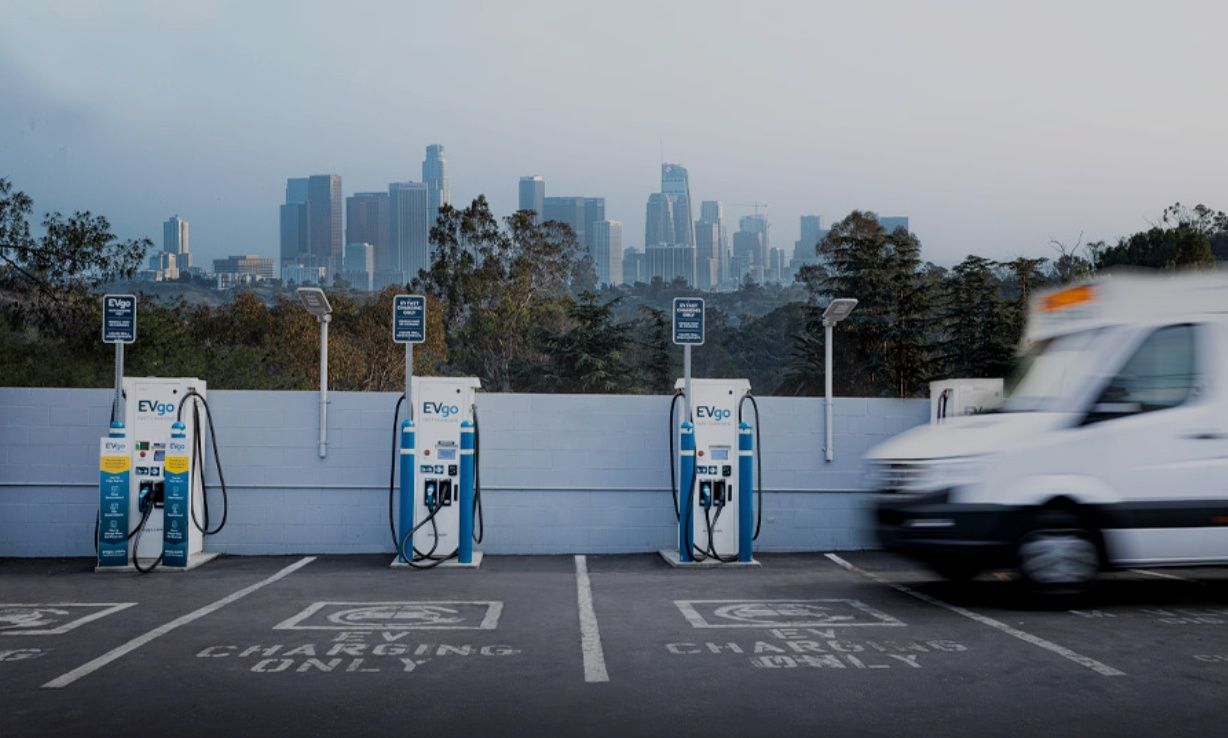 A white van is parked in a parking lot with a city skyline in the background.