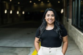 A woman is standing on a sidewalk with her hands in her pockets.