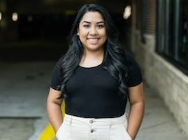 A woman is standing on a sidewalk with her hands in her pockets.