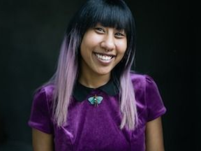 A woman with purple hair is wearing a purple shirt and smiling.
