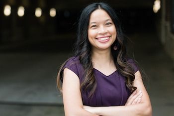 A woman in overalls is leaning against a car and smiling.