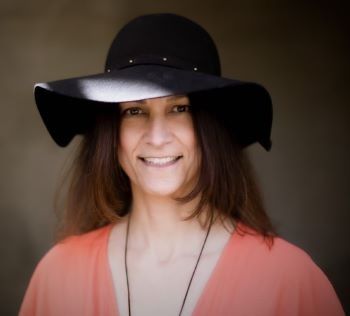 A woman wearing a black hat and a pink shirt is smiling.