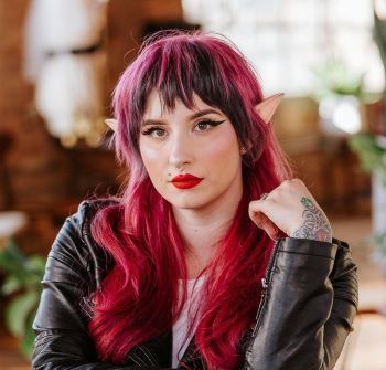 A woman with red hair and elf ears is wearing a black leather jacket.
