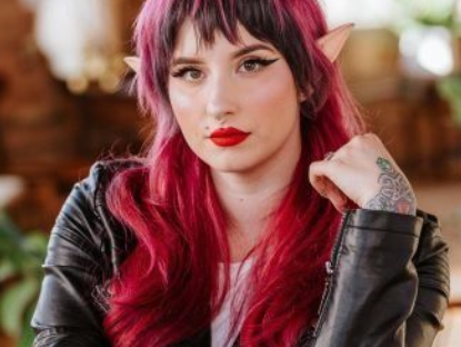 A woman with red hair and elf ears is wearing a black leather jacket.