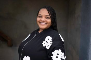 A woman wearing a black jacket with white flowers on the sleeves is smiling.