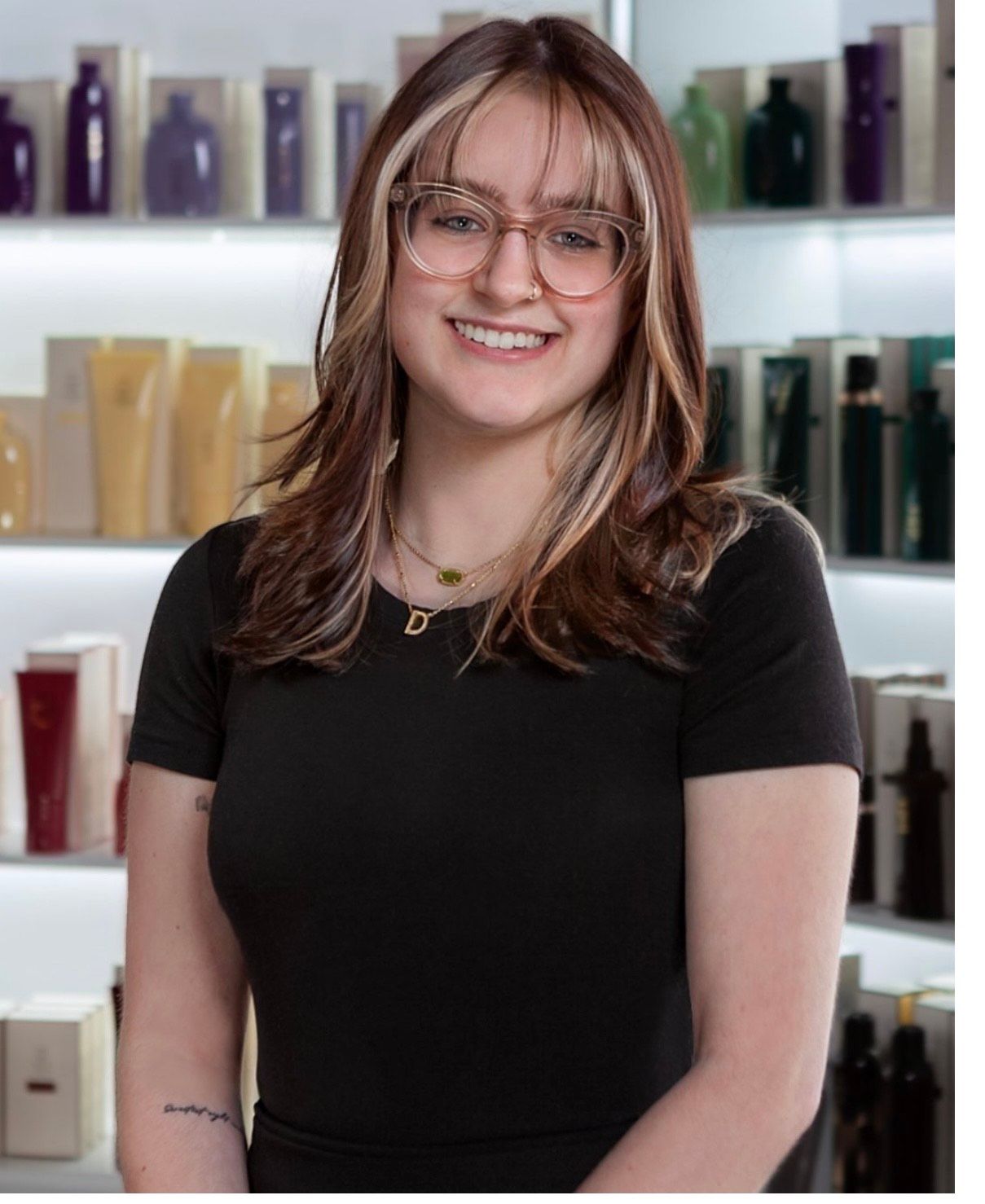 Woman with glasses and dark hair smiling in front of beauty product shelves.