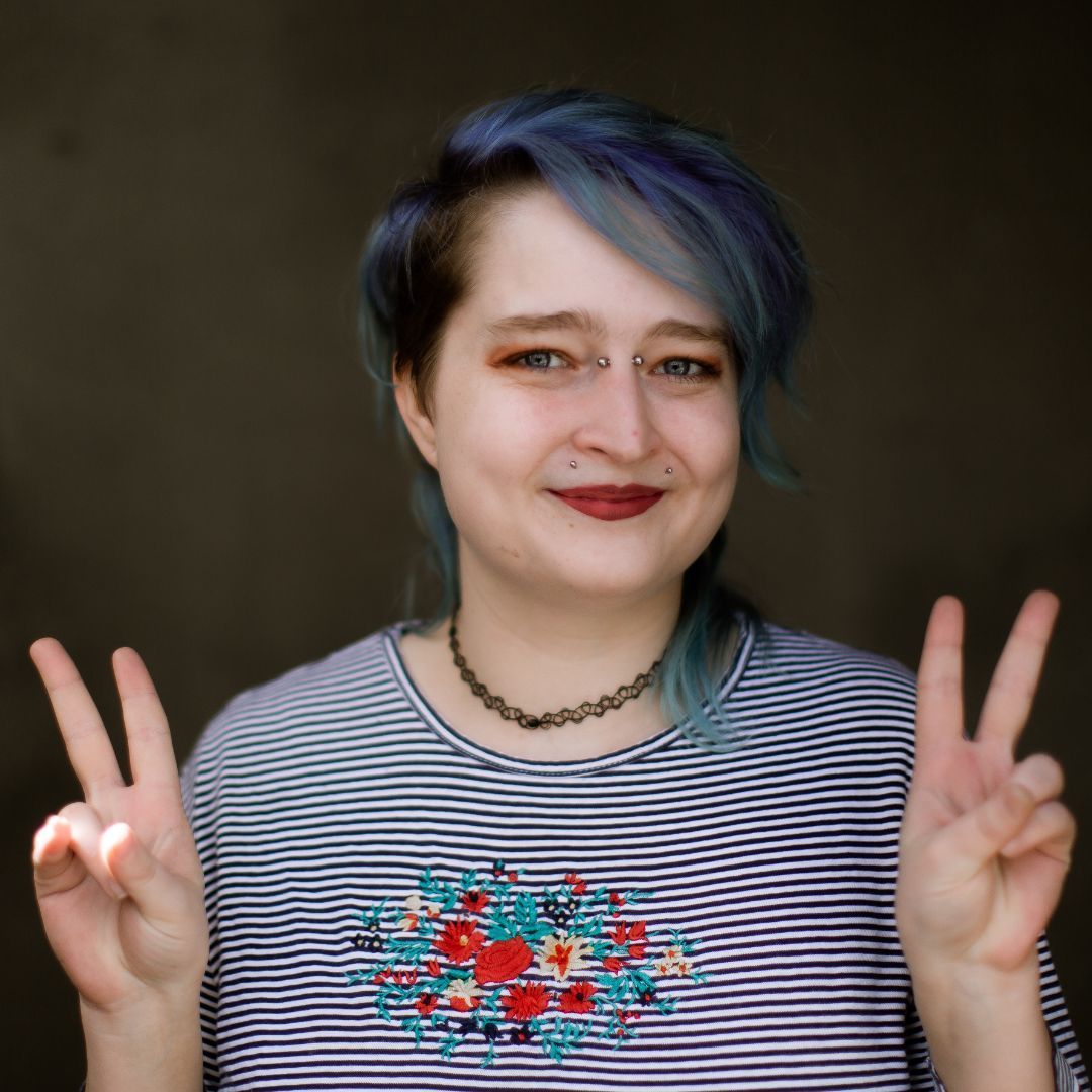A woman with blue hair is giving a peace sign