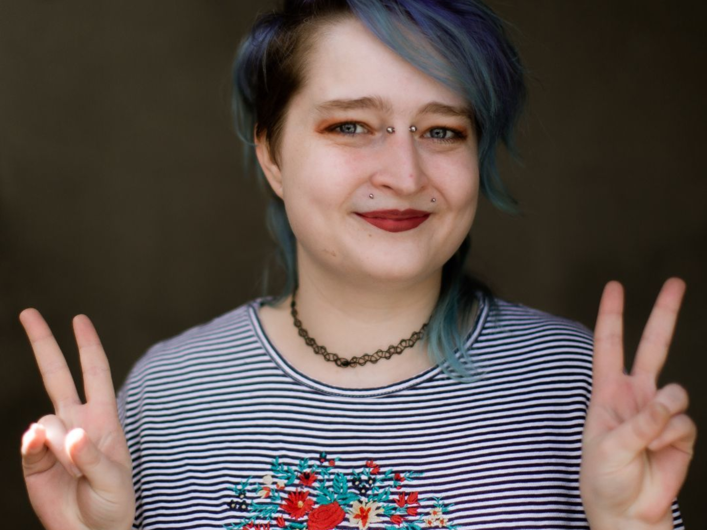 A woman with blue hair is giving a peace sign