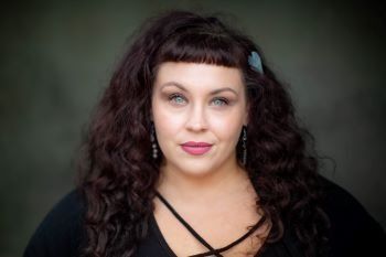 A woman with curly hair is wearing a black shirt and earrings.