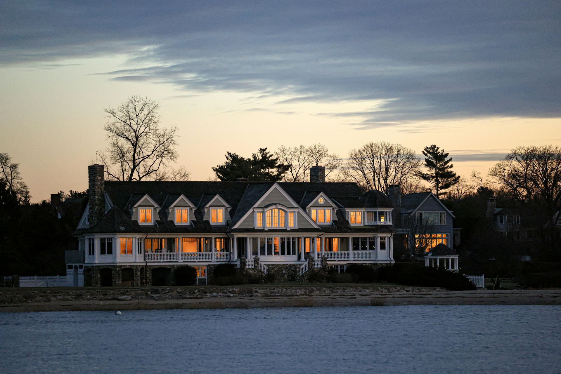 A large house sits next to a body of water at sunset