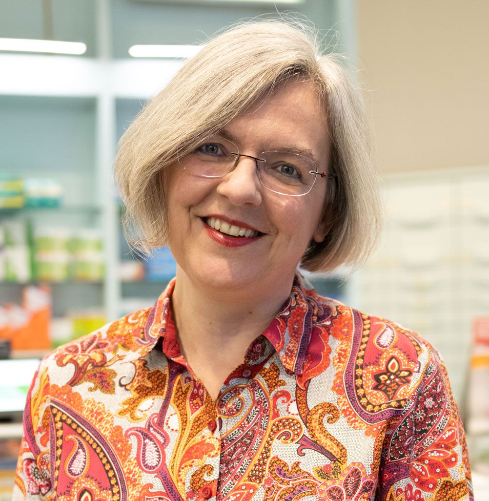 Eine Frau mit Brille und buntem Hemd lächelt in die Kamera.