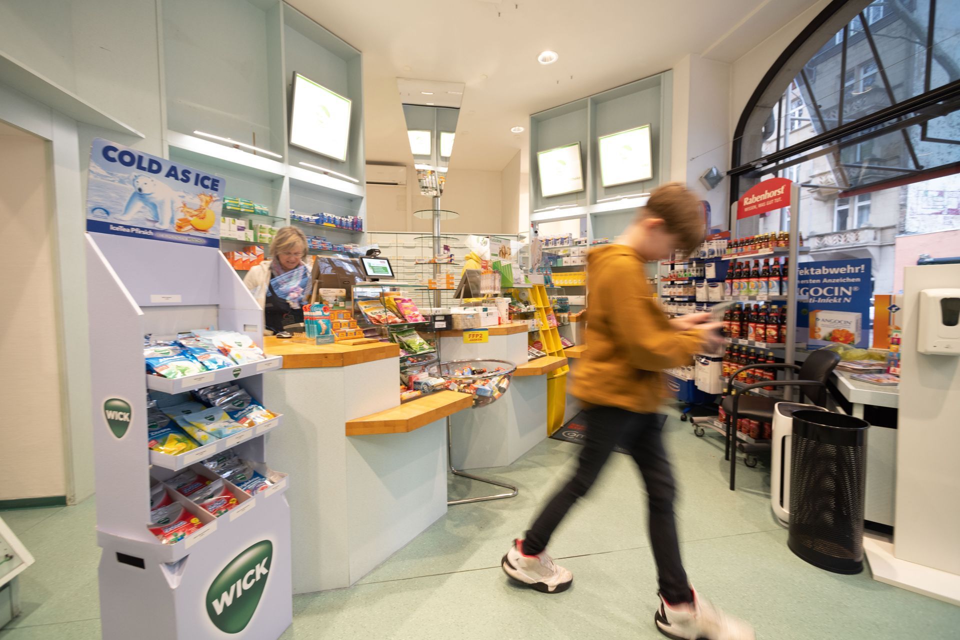 Ein Mann geht durch eine Apotheke und schaut auf sein Telefon.