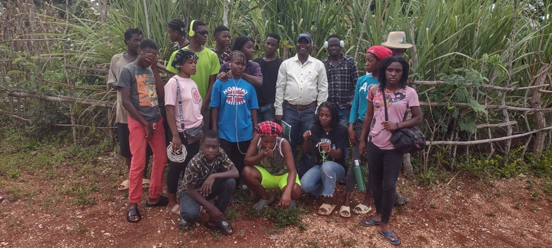 A group of young people posed in front of greenery and a small fence.