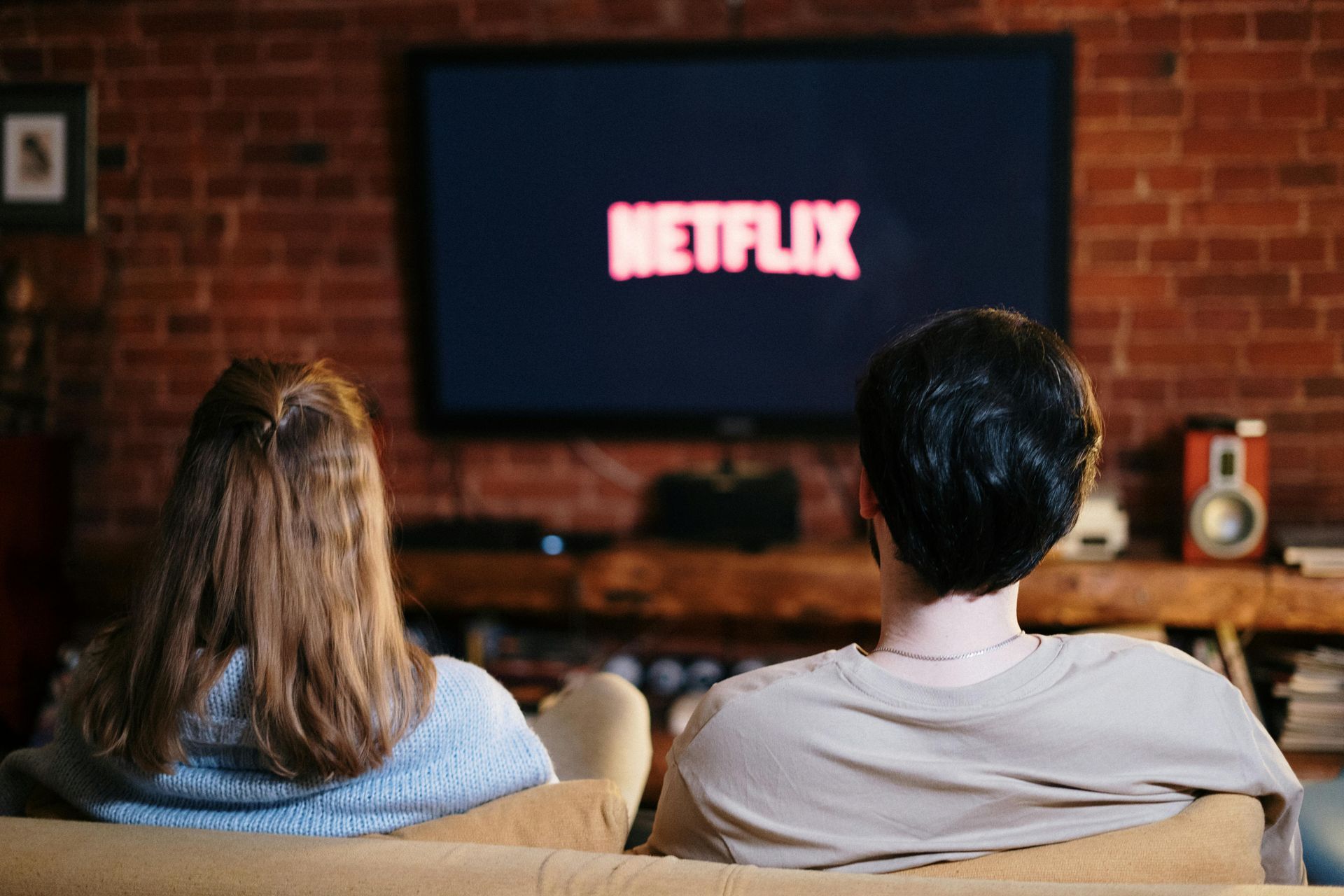 A man and a woman are sitting on a couch watching netflix on a television.