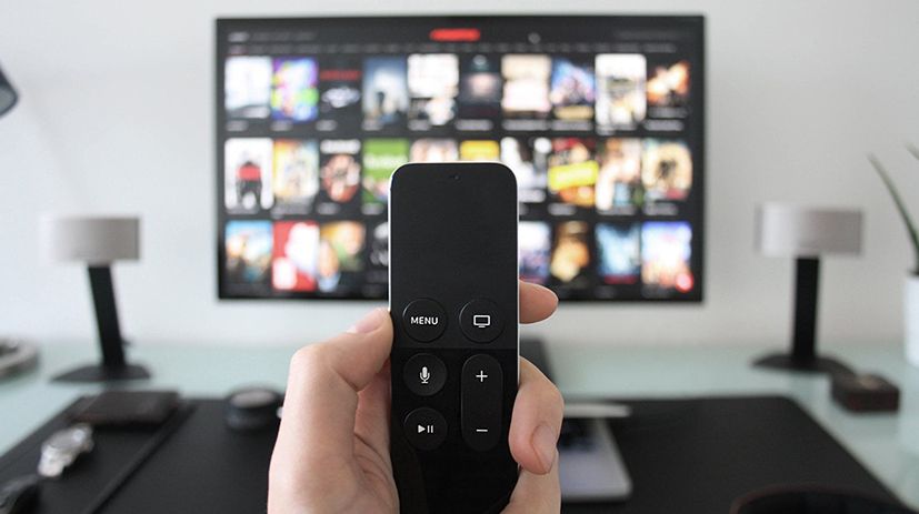 A person is holding a remote control in front of a television.