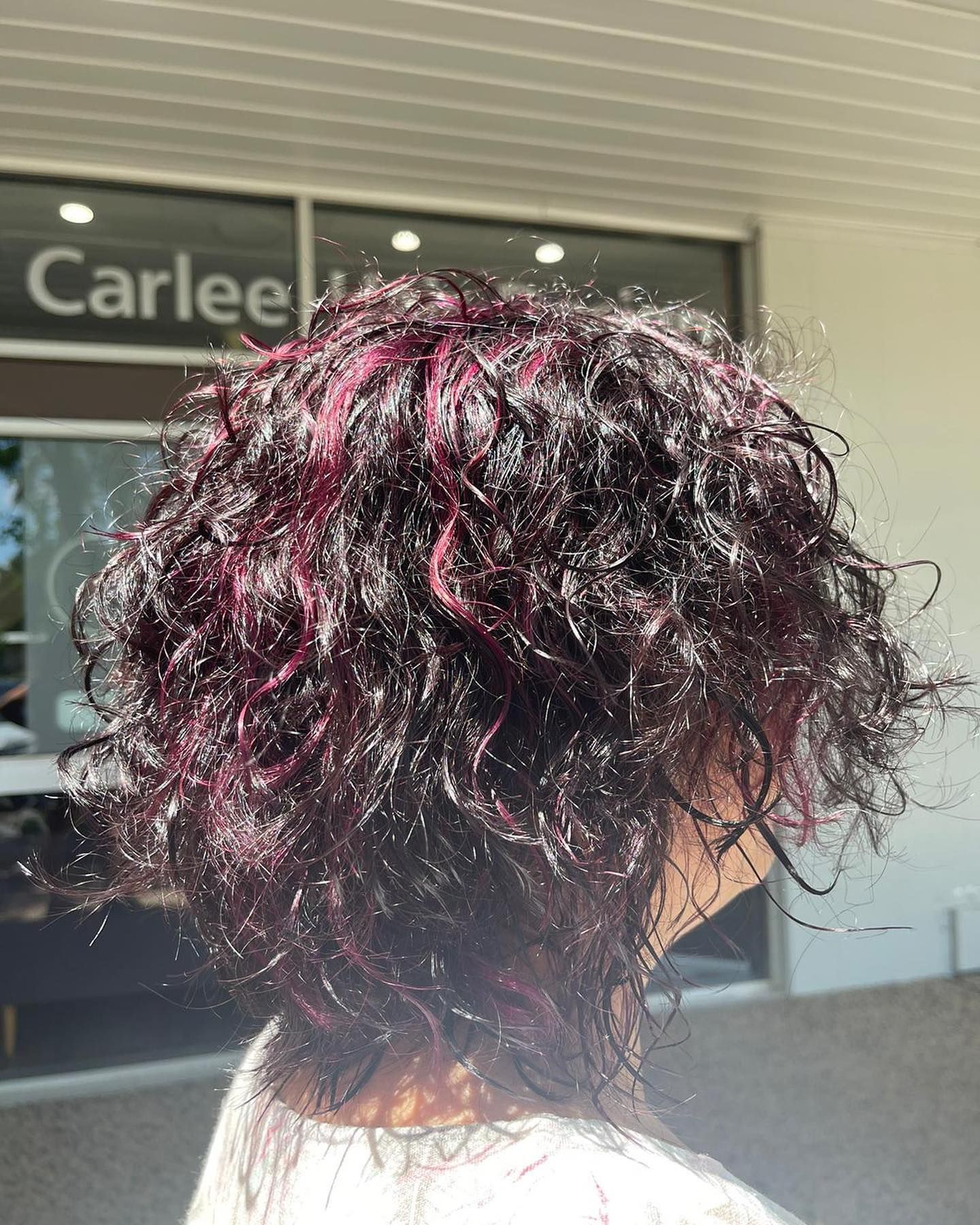 A woman with curly hair is standing in front of a carlee hair salon — Carlee Hair Design In Anula, NT