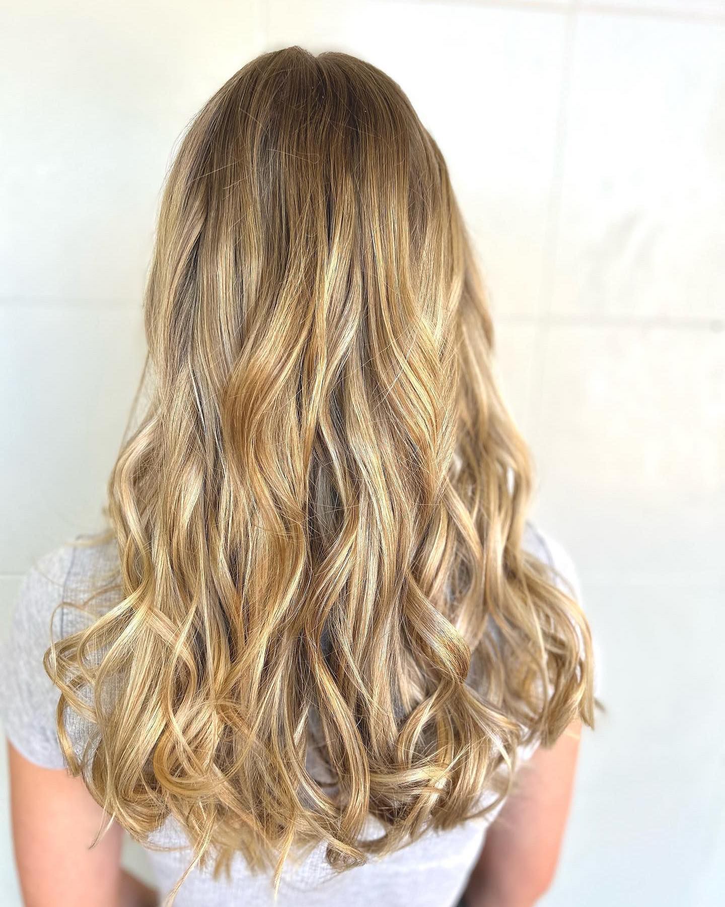 A woman with long blonde curly hair is wearing a white shirt — Carlee Hair Design In Anula, NT