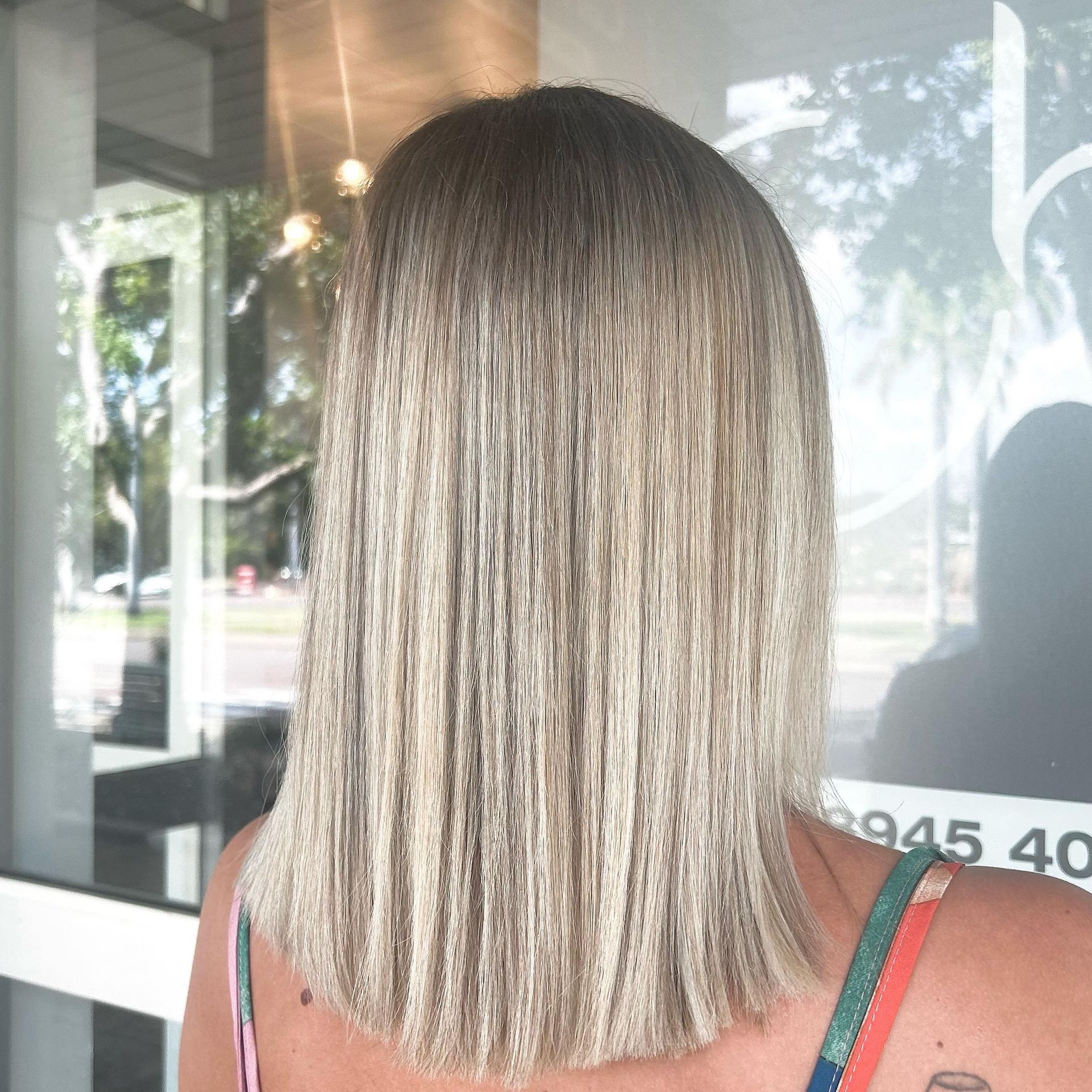A woman with straight blonde hair is standing in front of a hair salon — Carlee Hair Design In Anula, NT