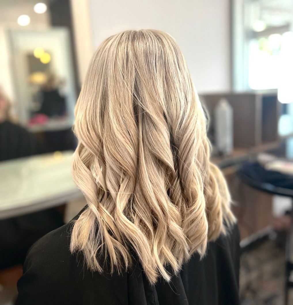A woman with blonde hair that has been curled is sitting in a salon chair — Carlee Hair Design In Anula, NT