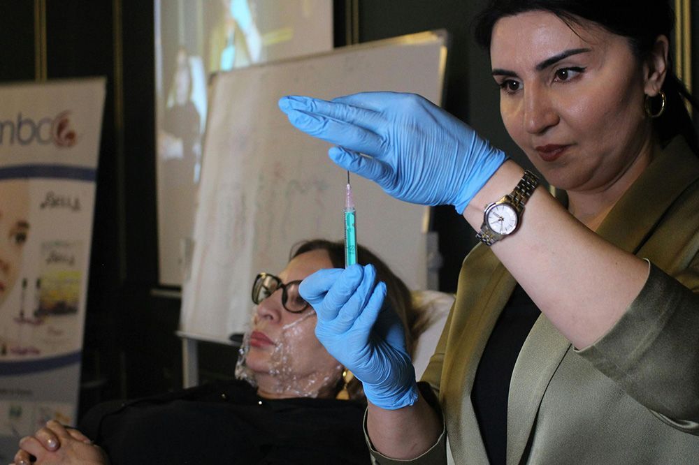A woman wearing blue gloves is holding a syringe in front of a patient.