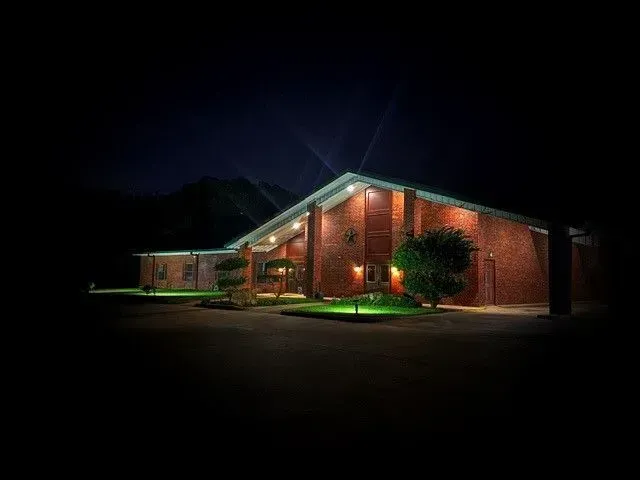 A single-story brick building illuminated by exterior lights against a dark night sky, surrounded by manicured lawn.
