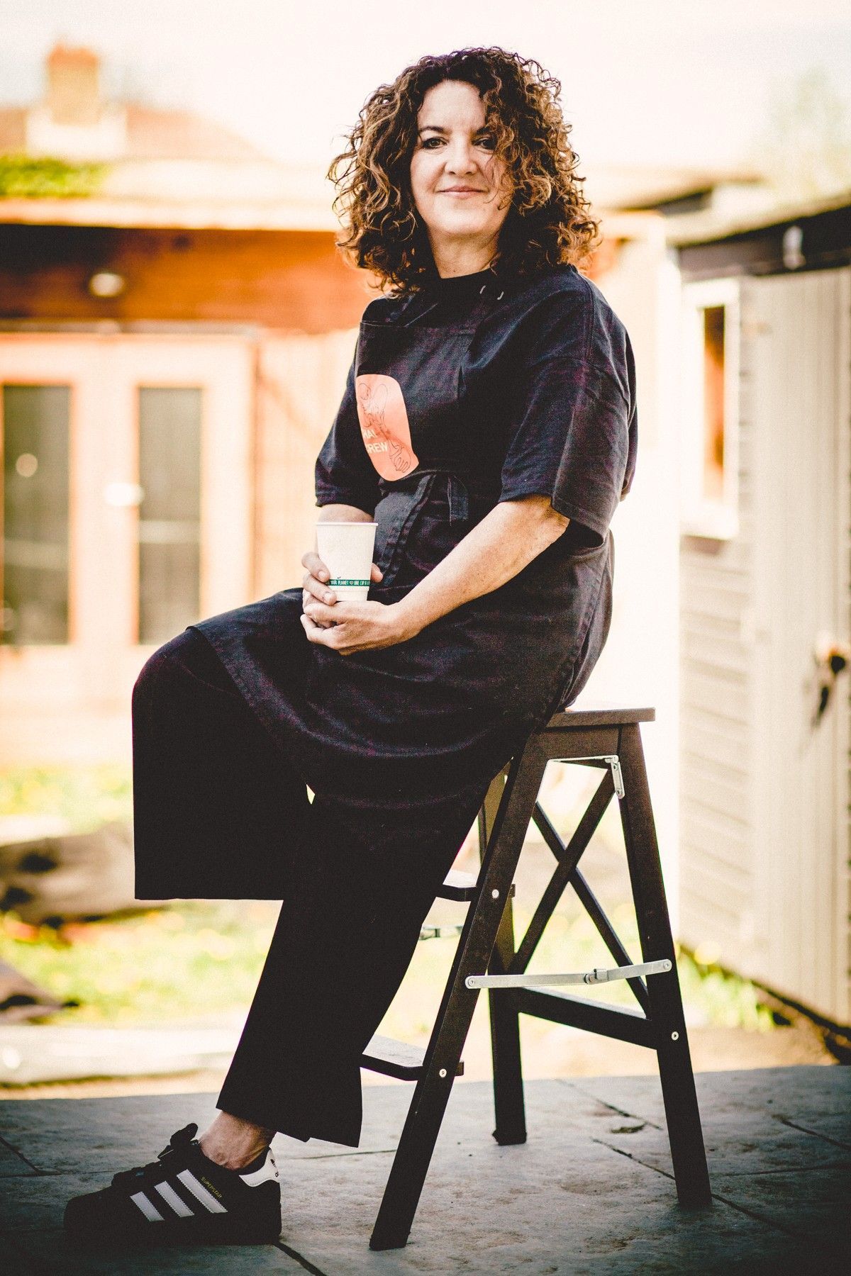 Woman with curly red hair operates a wooden vending cart on a path in a park, with a black awning overhead.