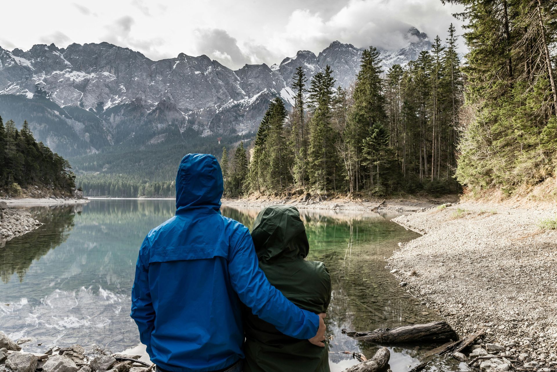 A man and a woman are standing next to a lake with mountains in the background.