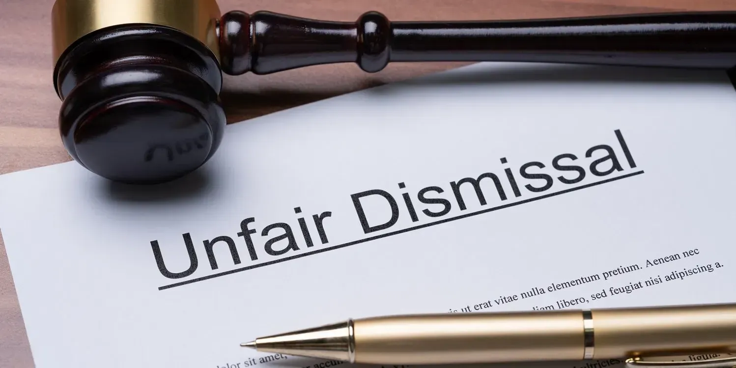 Wooden gavel and golden ballpen lying down in a printed document titled Unfair Dismissal.