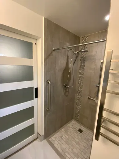 Accessible shower with grab bars, gray tile walls, and a sliding door.