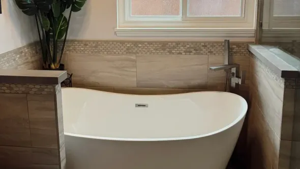 Freestanding white bathtub in a bathroom, with tile walls and a window.