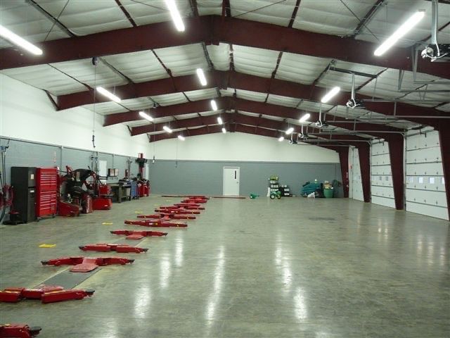 Wooden deck with seating area under a pergola. String lights, gray siding, and green lawn.