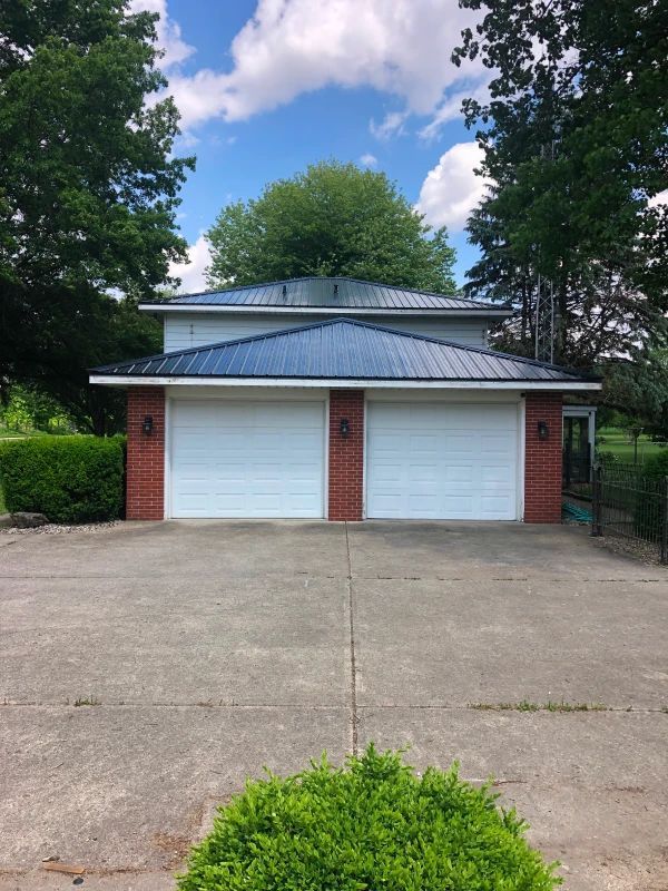 Tan house with gray shingled roof, blue trim, and brick chimney against a blue sky with clouds.