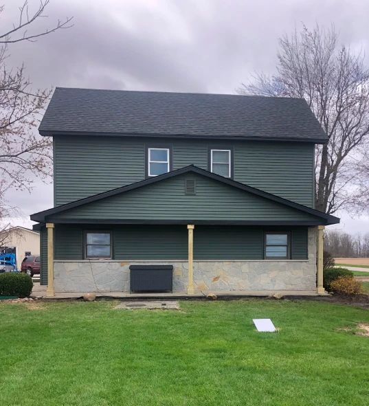 House with gray roof, tan siding, and white trim against a blue sky.