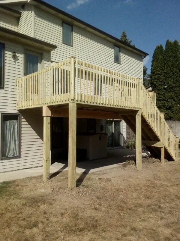 Wooden deck with seating area under a pergola. String lights, gray siding, and green lawn.