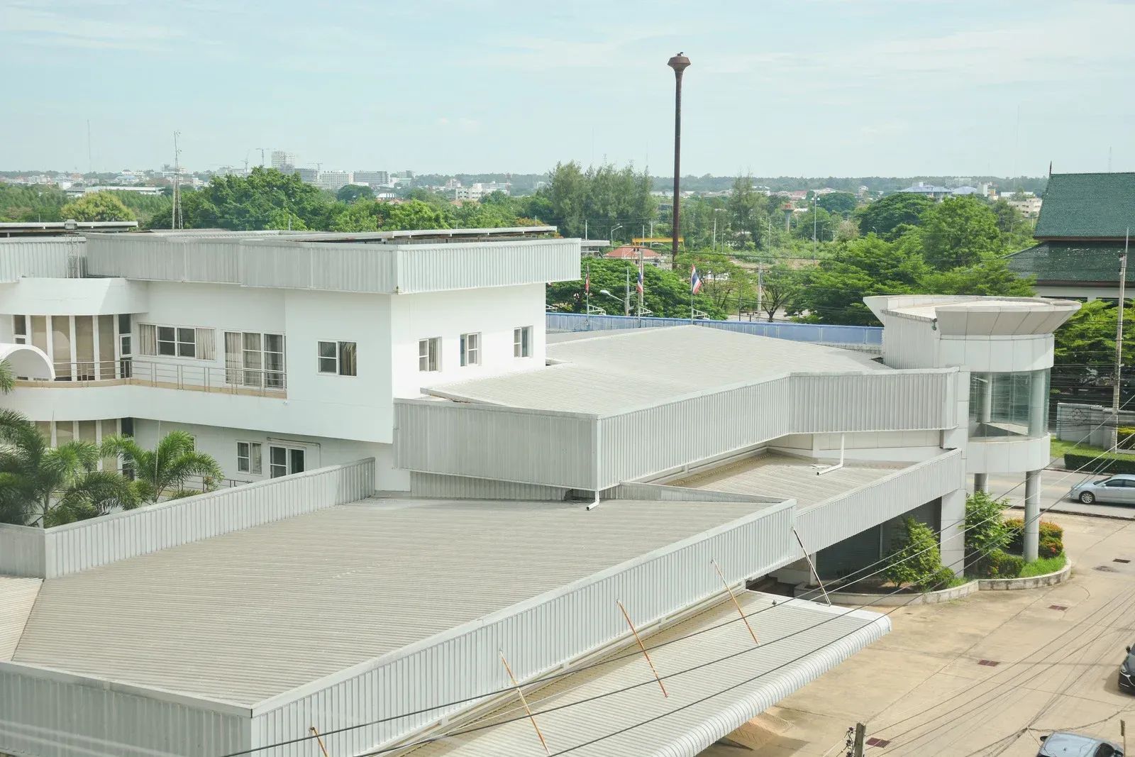 White building with flat roofs, trees, and distant cityscape under a cloudy sky.