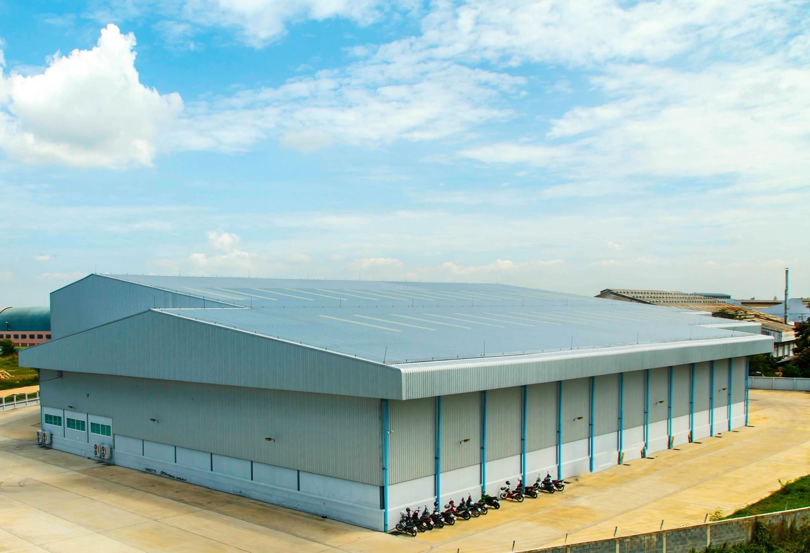 Large industrial warehouse with gray metal siding and roof, blue sky background.