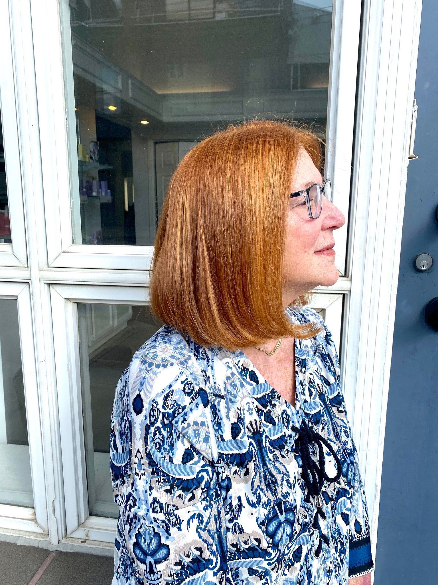 A woman with red hair and glasses is standing in front of a window.
