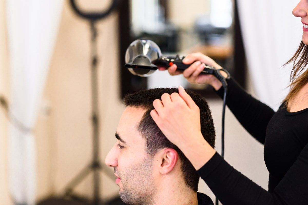 A woman is blow drying a man 's hair in a salon.