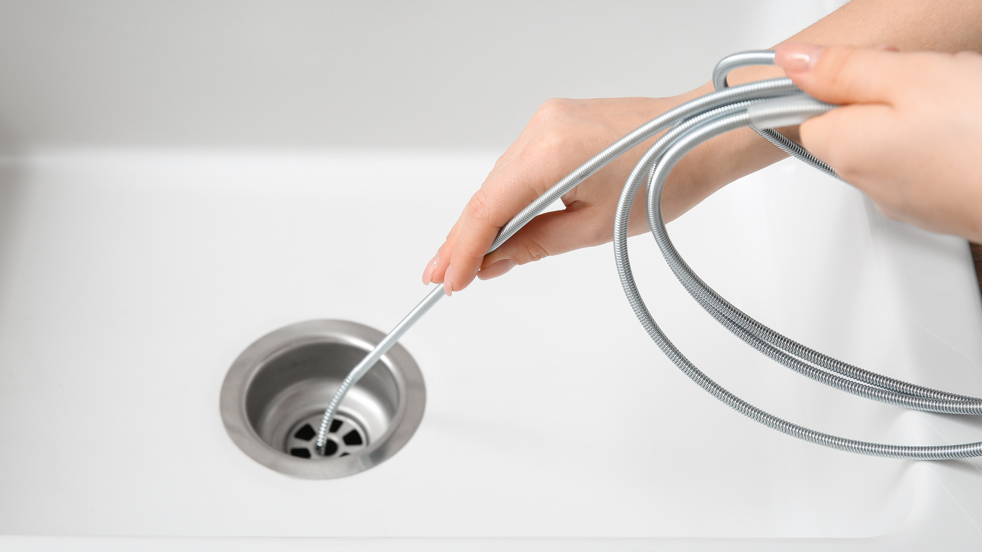 Person using a drain snake tool to unclog a kitchen sink.