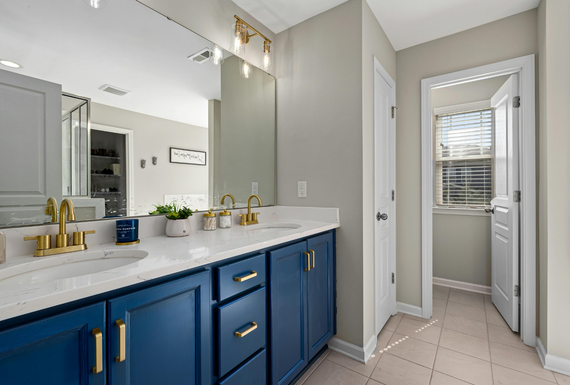 Blue bathroom vanity with gold fixtures, white countertop, and doorway to a light-filled space.