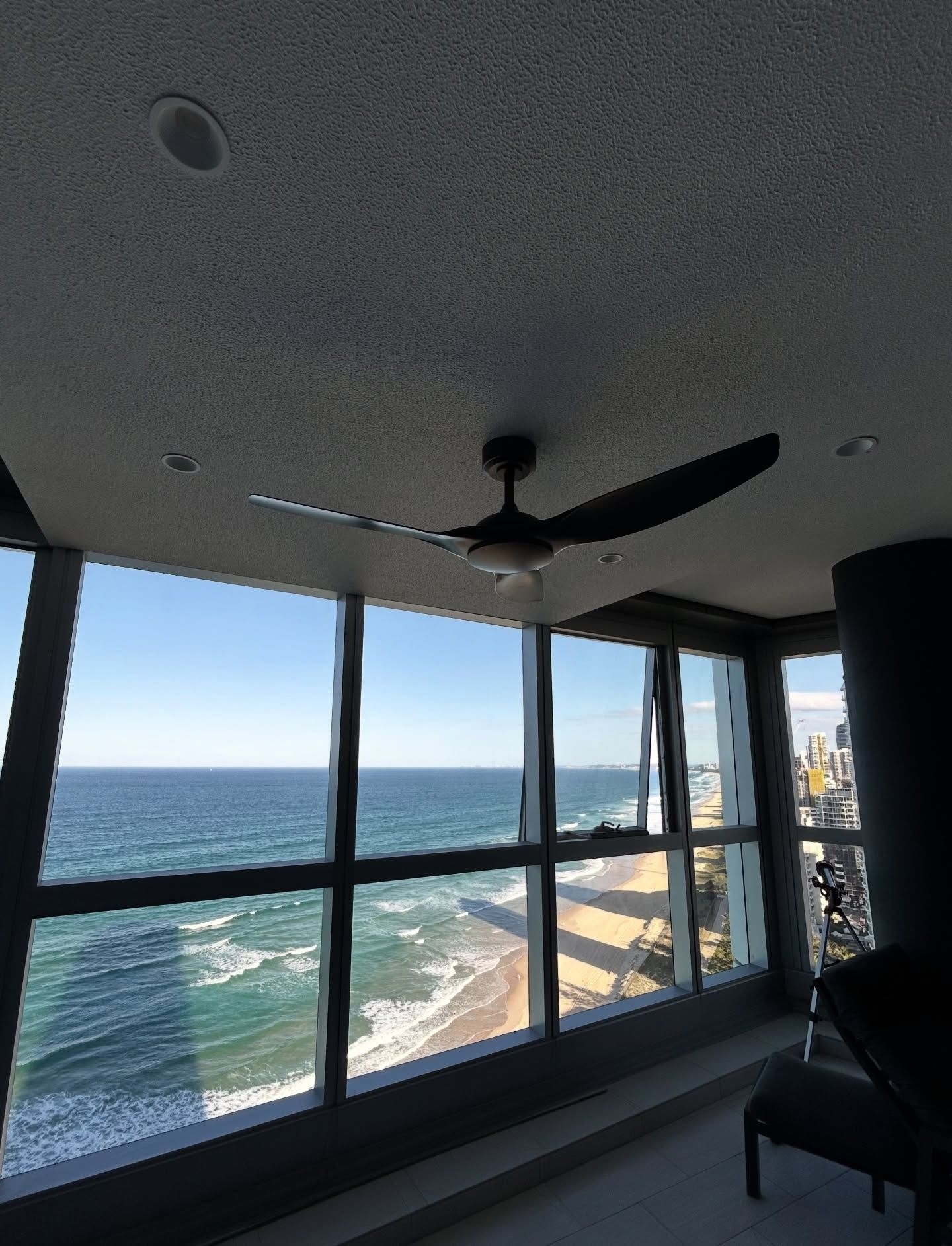 Modern apartment interior with large windows overlooking the ocean and shoreline, black ceiling fan above — BTM Electrical & Air in Burleigh Waters, QLD