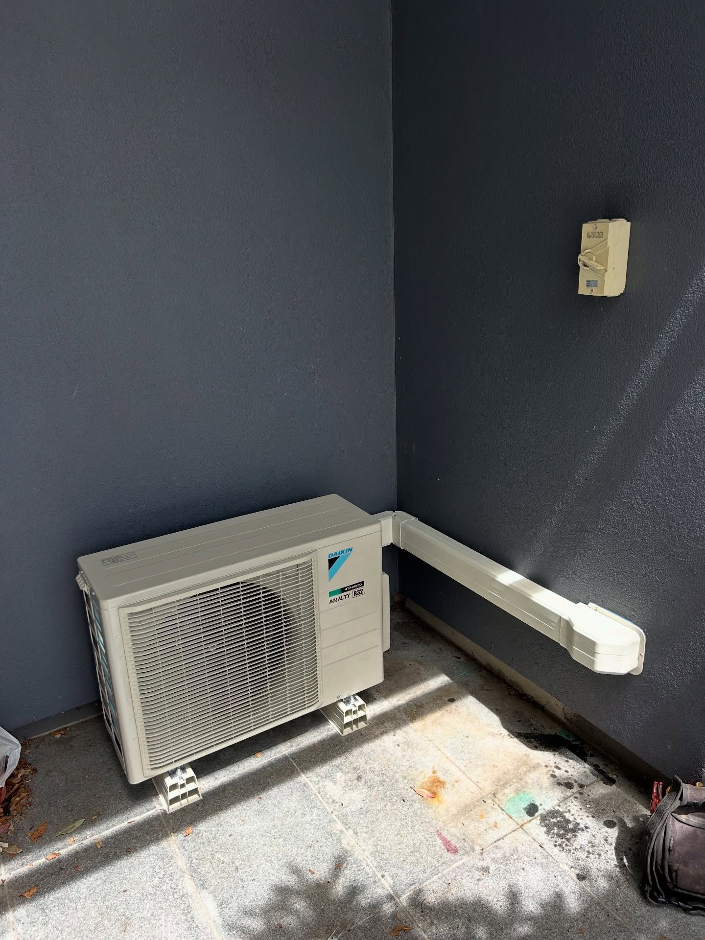 A Beige Outdoor Air Conditioning Unit Sits on a Concrete Patio — BTM Electrical & Air in Robina, QLD