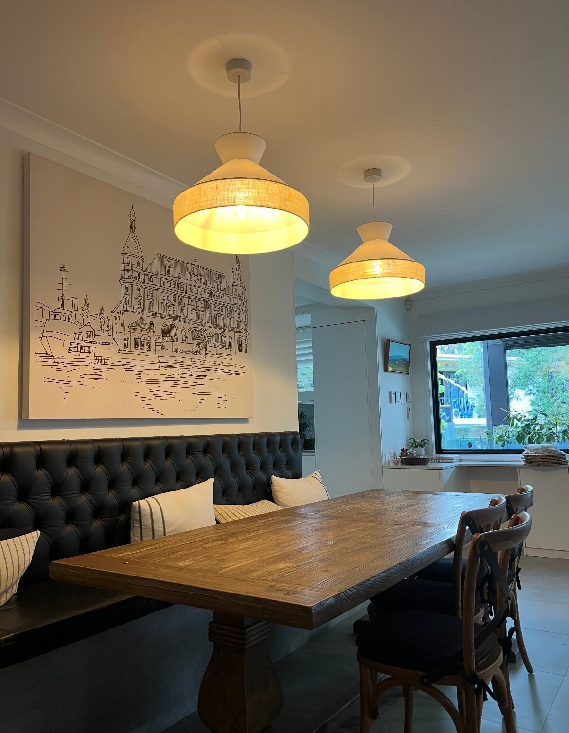 A dining area with a long wooden table, tufted black bench, and matching chairs beneath two modern dome pendant lights. — BTM Electrical & Air in Burleigh Heads, QLD