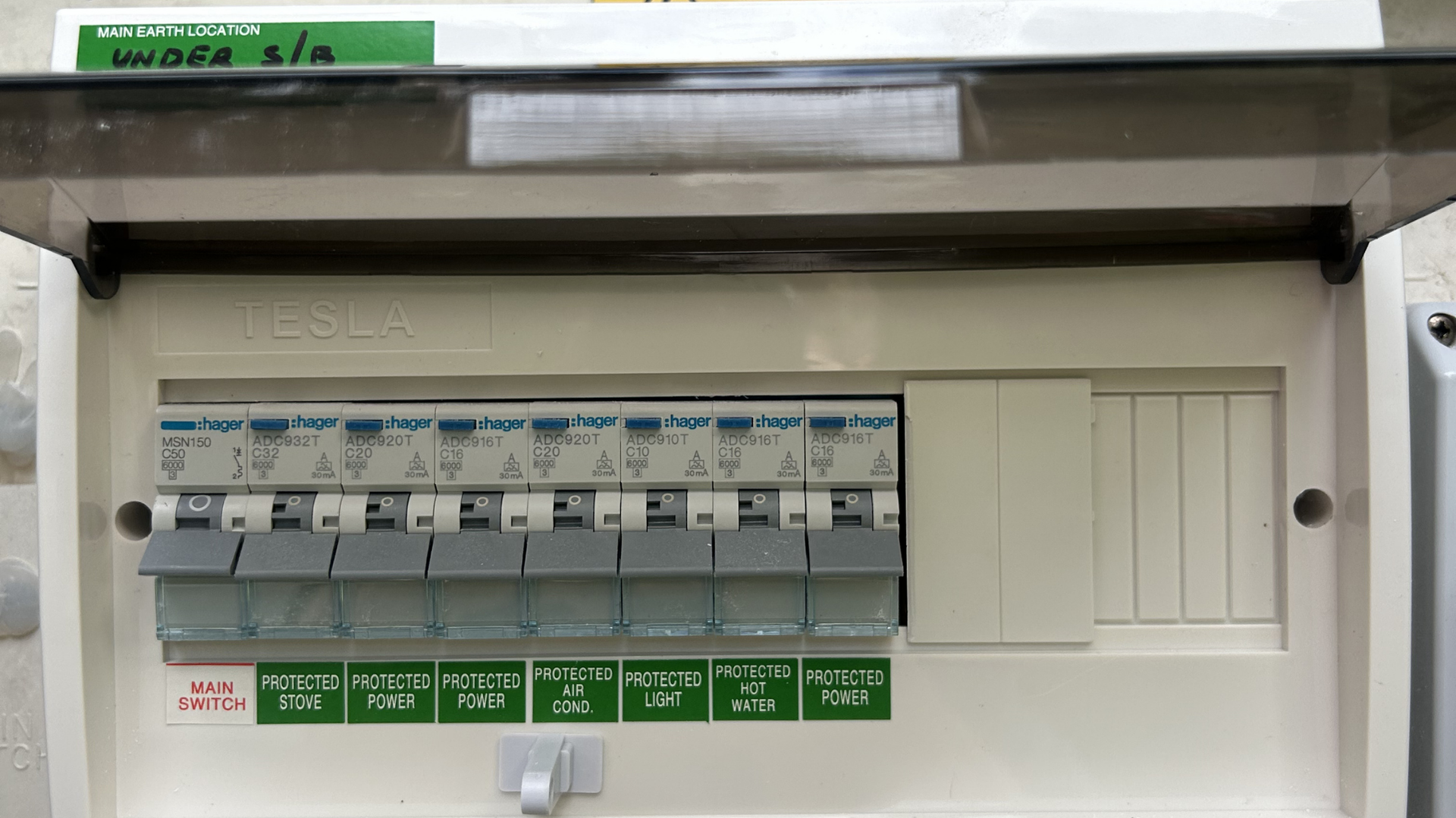 Wall-mounted electrical consumer unit with circuit breakers and green labels, under an open clear plastic cover. — BTM Electrical & Air in Southport, QLD